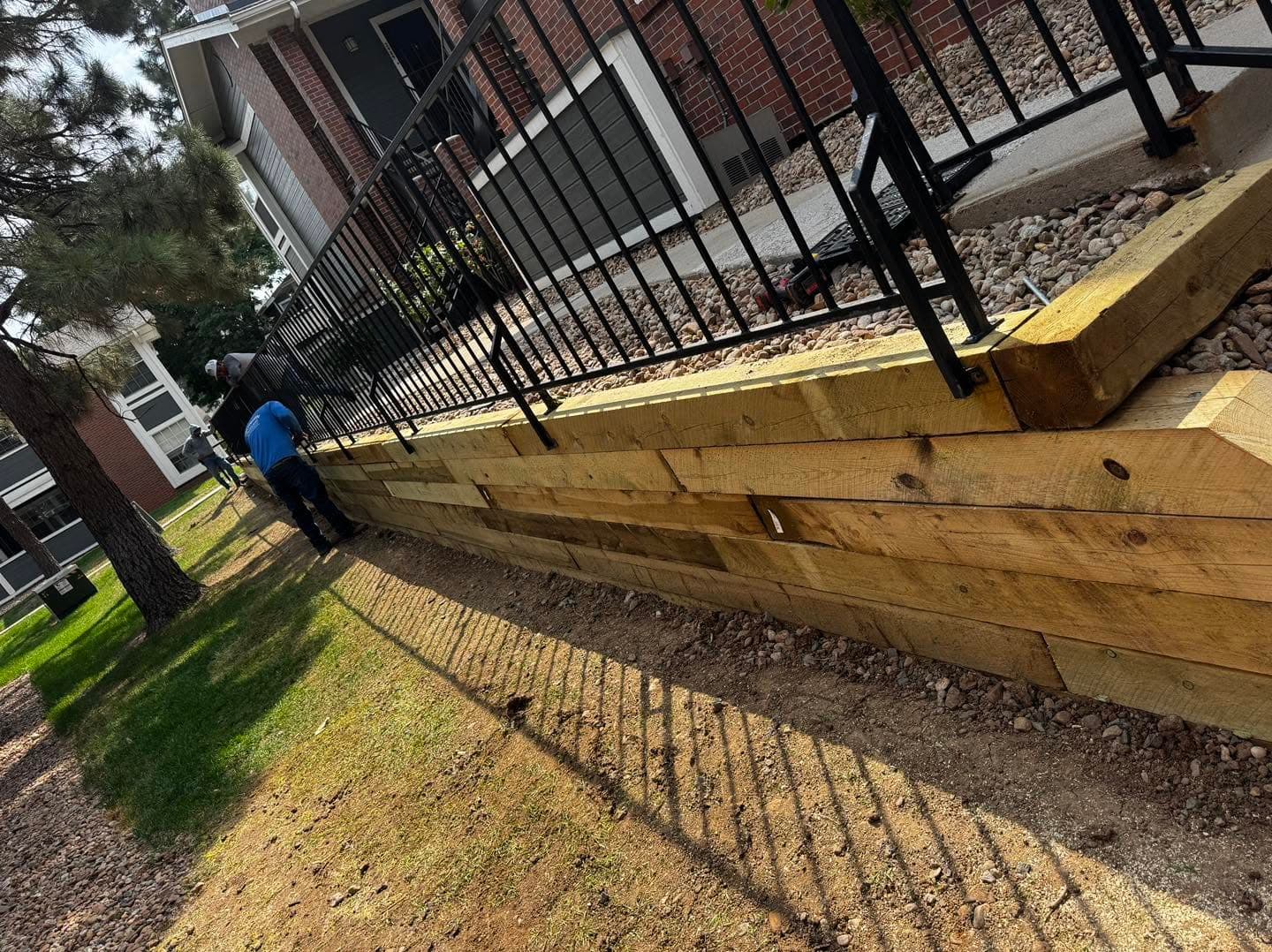 Wooden retaining wall construction with metal railing and stone foundation
