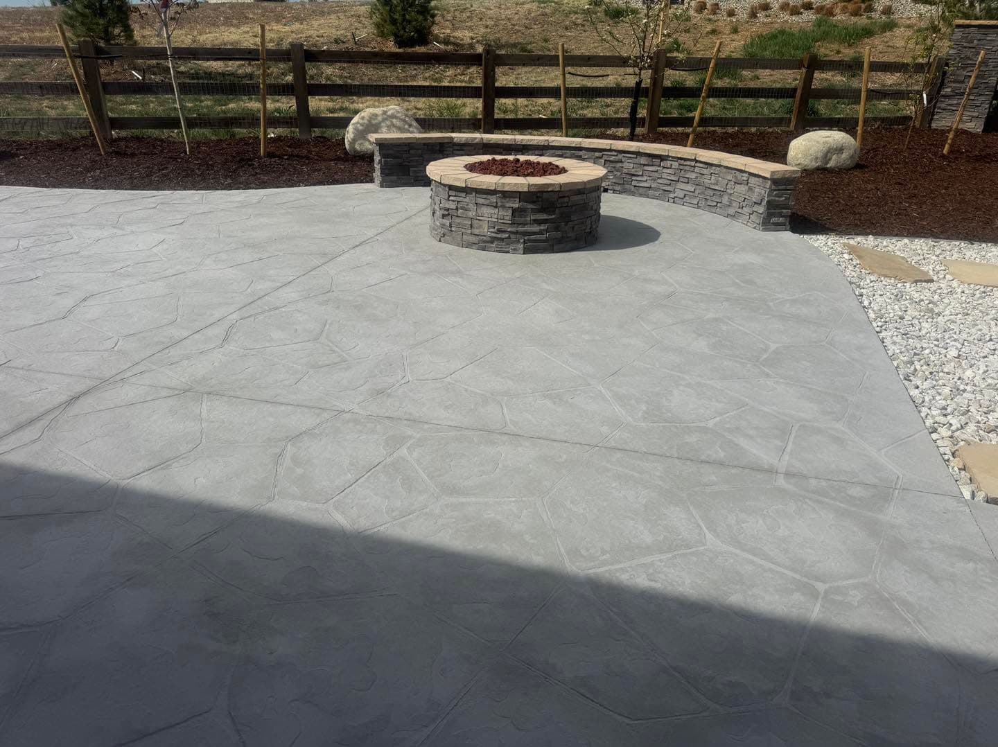Concrete patio with fire pit, rock seating, and decorative gravel