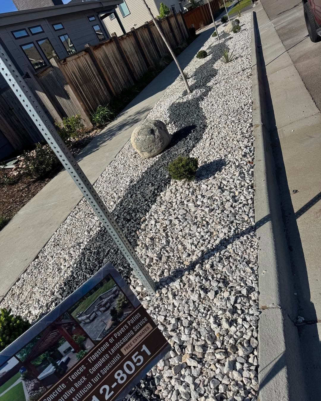 White gravel bed with dark fence, concrete curb, and river stones
