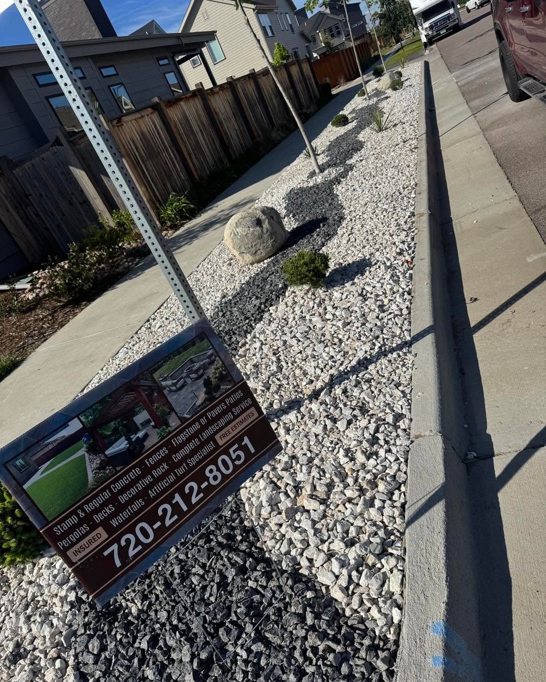 White gravel landscape with decorative stones, concrete curb, and dark fence