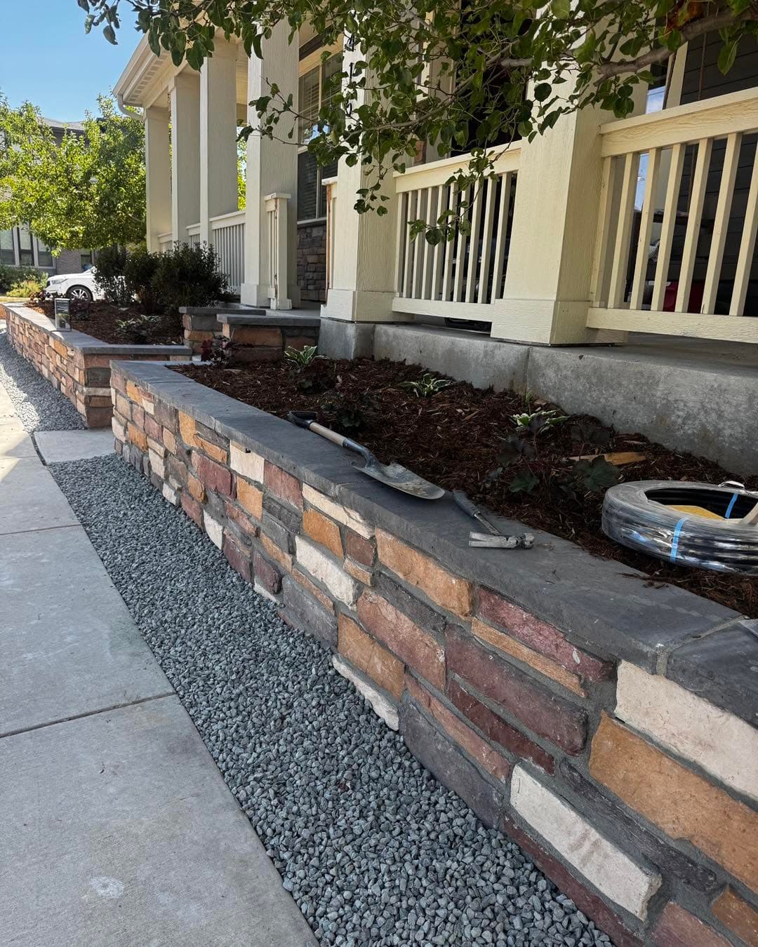 Front yard with brick retaining wall, mulch beds, and gravel borders