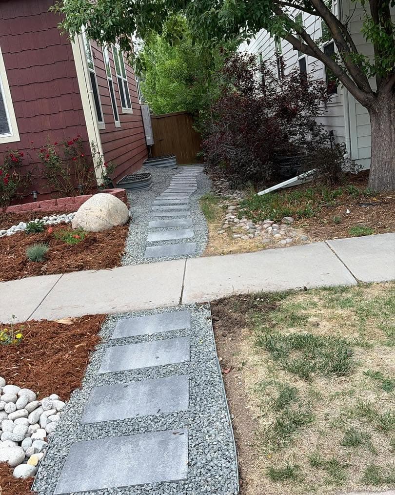 Concrete stepping stone path through mulch beds with boulders